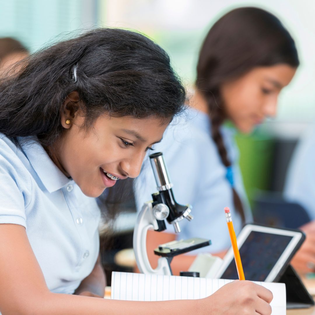 girl taking notes in a science lab next to a microscope